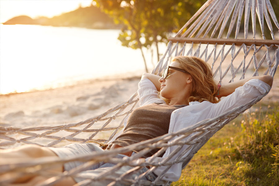 A woman gazing at the ocean while lounging in a rope hammock.