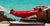 A man lounging in a red hammock with stand on a sunny day in front of the ocean.
