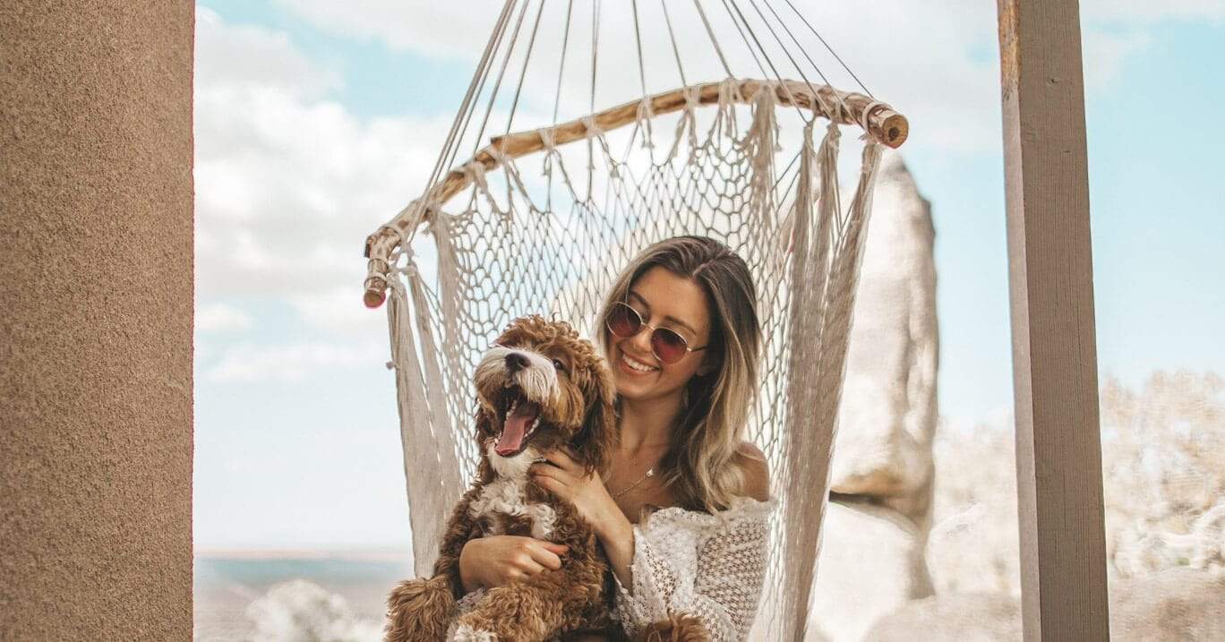 A young woman sits in a Brazilian hammock chair holding her dog.