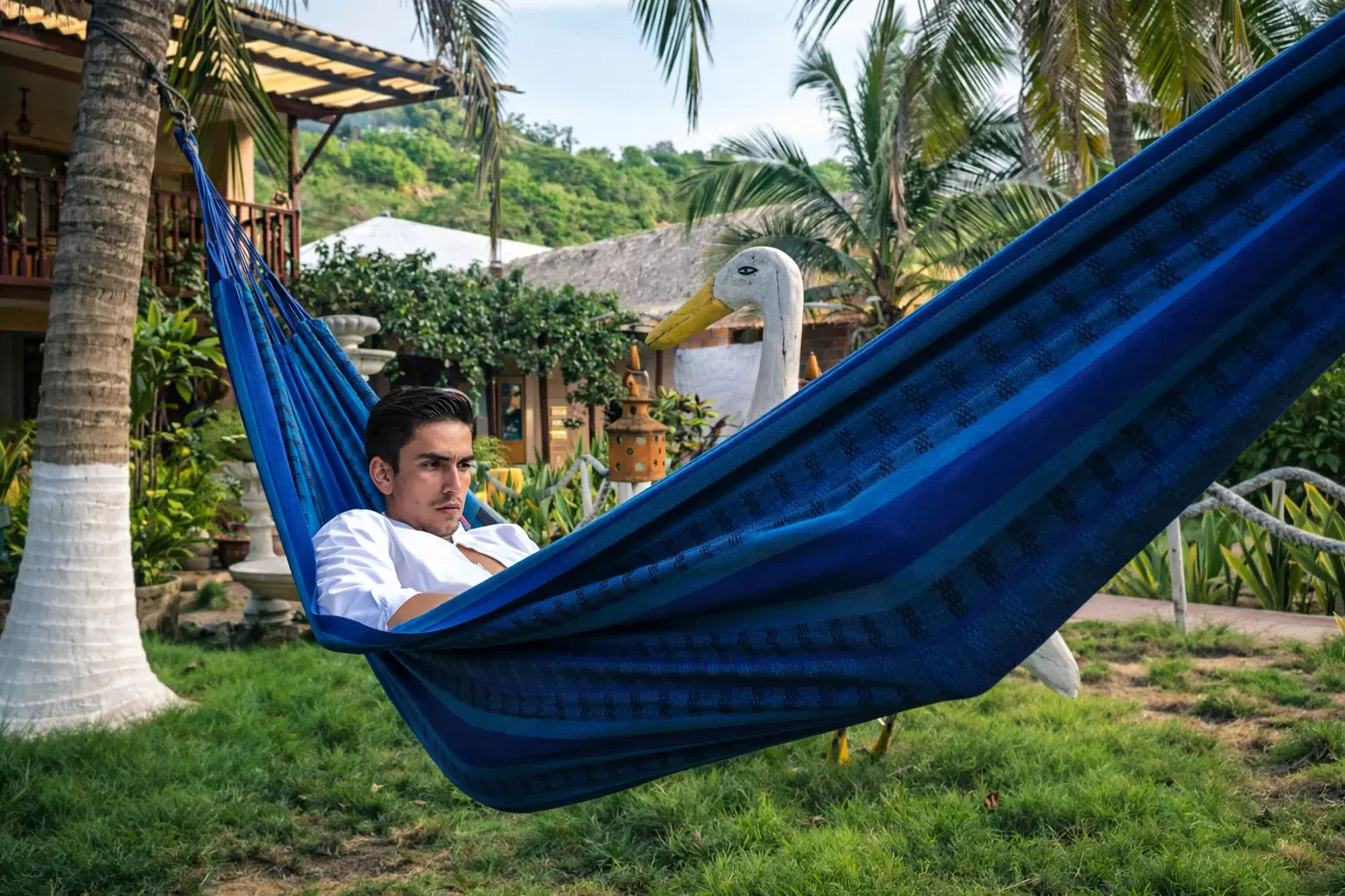 Person relaxing in a blue hammock with a duck nearby, surrounded by greenery. 20190