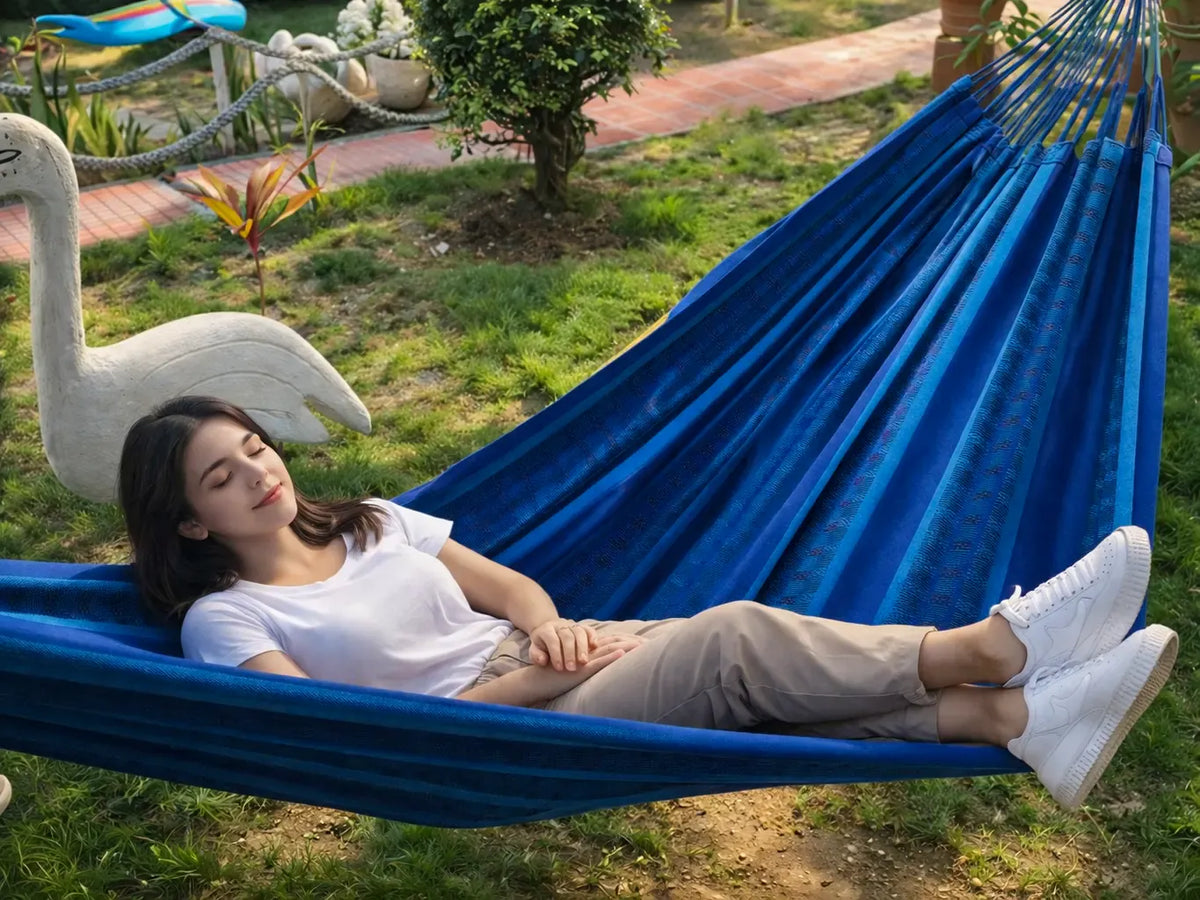 Woman relaxing in a blue hammock outdoors with greenery and a swan statue in the background. 20190