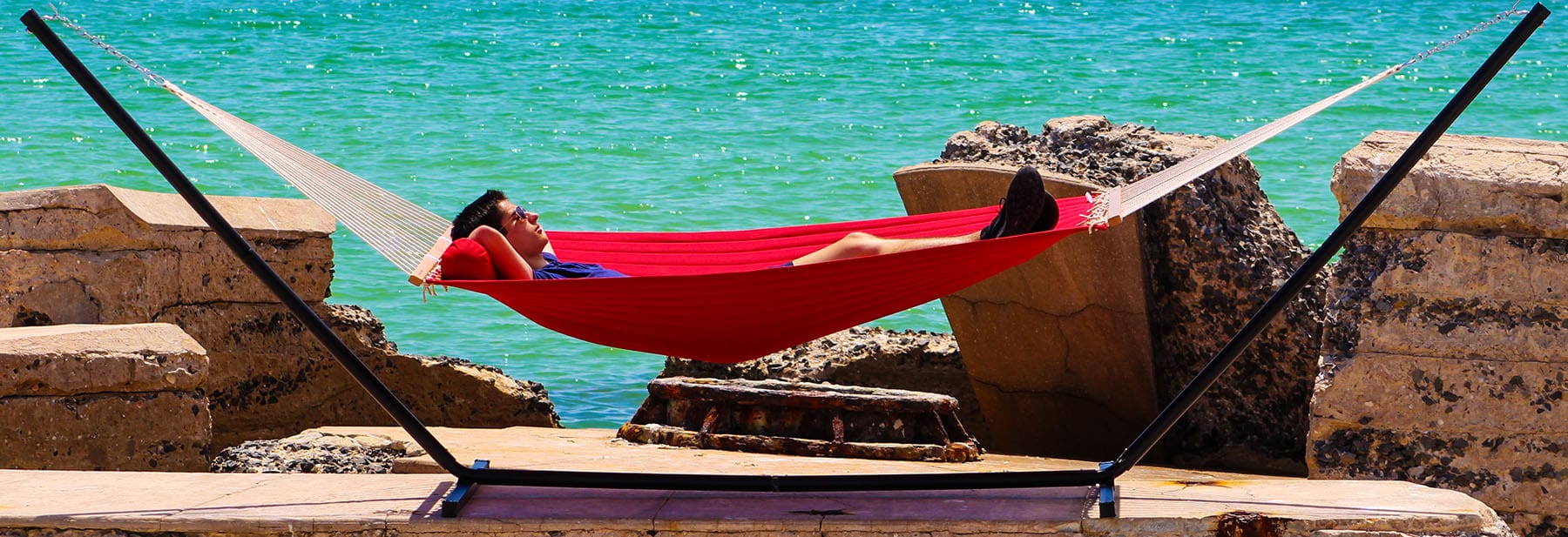 Young man in a red hammock with metal stand by the ocean