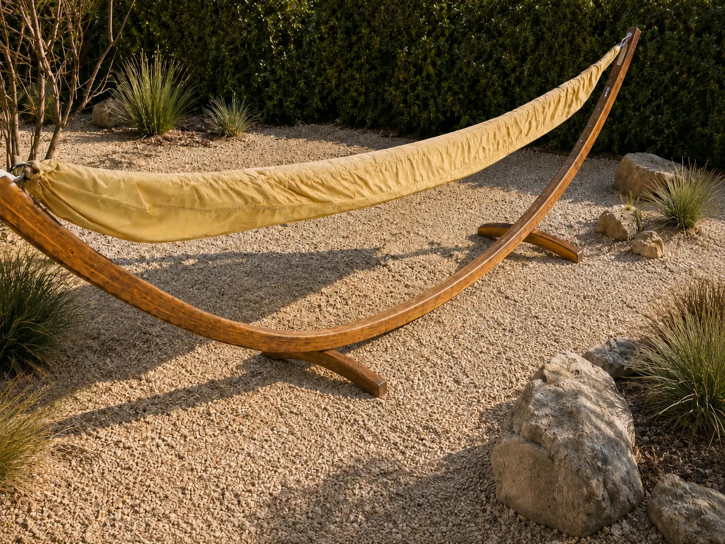 Yellow hammock on a wooden stand in a natural outdoor setting with rocks and plants.