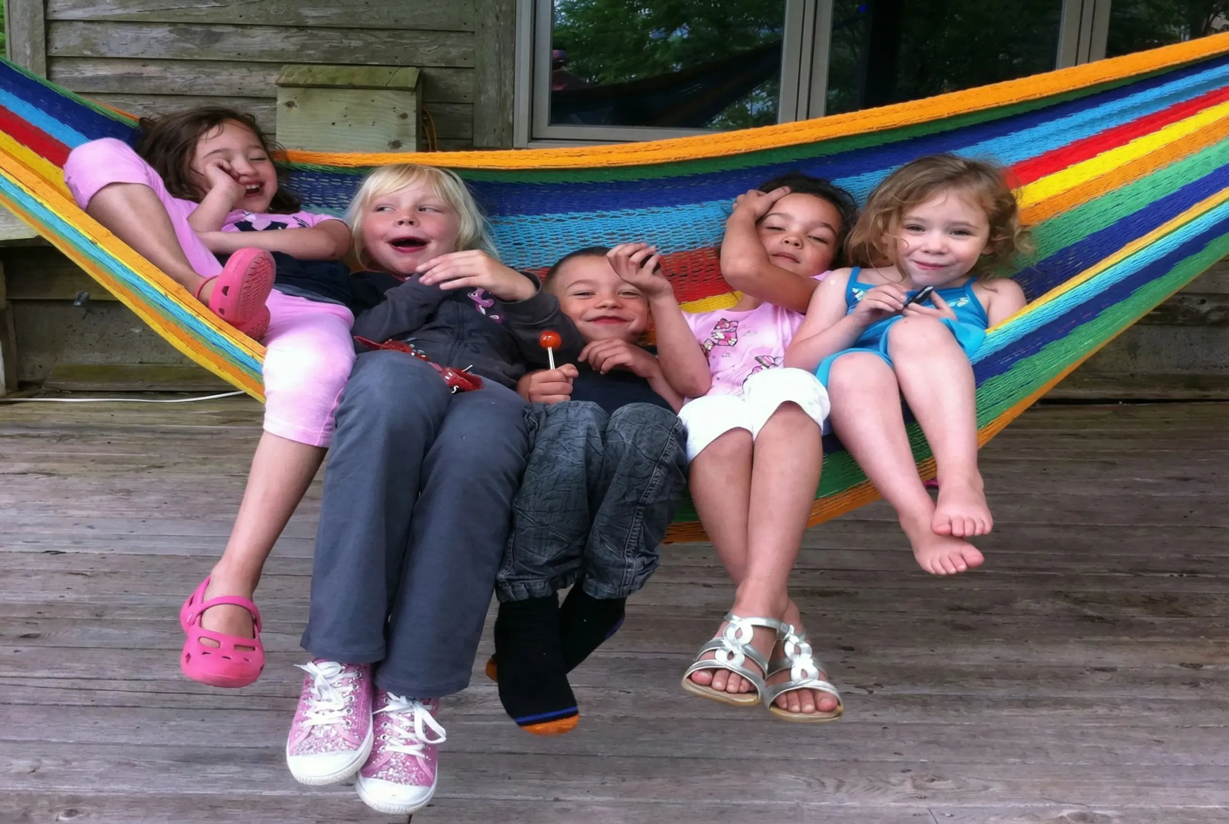 Children sitting in a colorful hammock on a wooden deck #24-MHXLTC-H