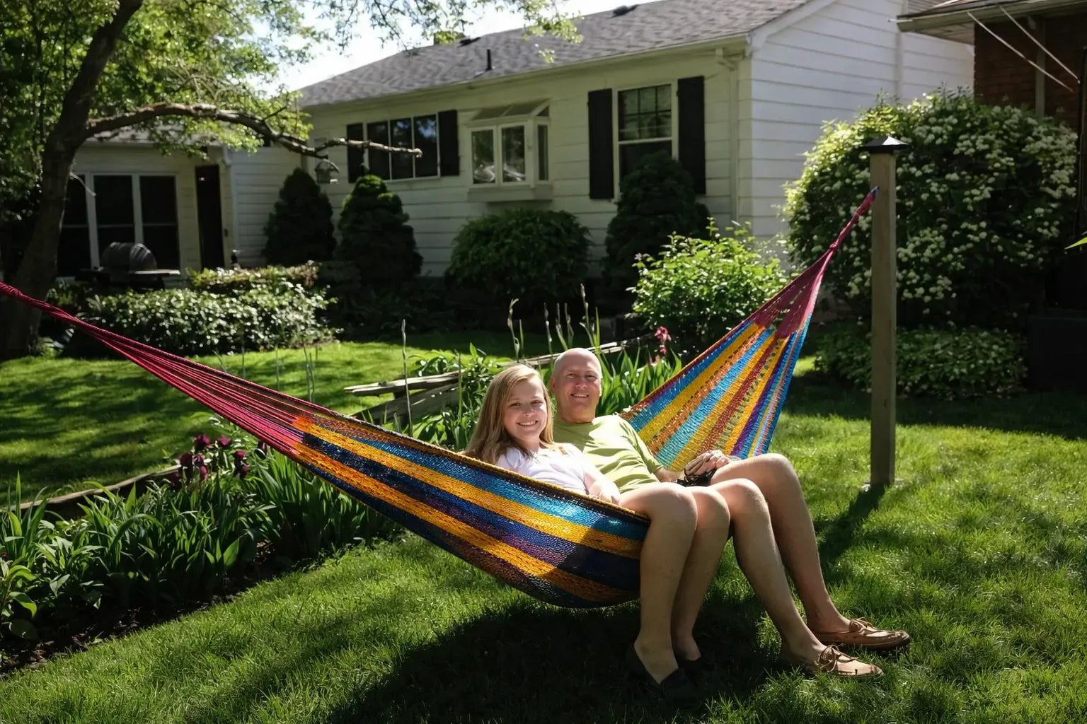 Two people sitting in a colorful hammock in a backyard. #24-MHXLTC-H