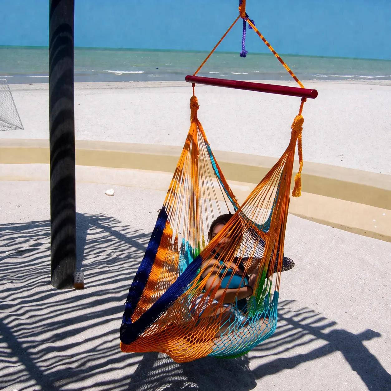 Person sitting in a colorful hammock by the beach