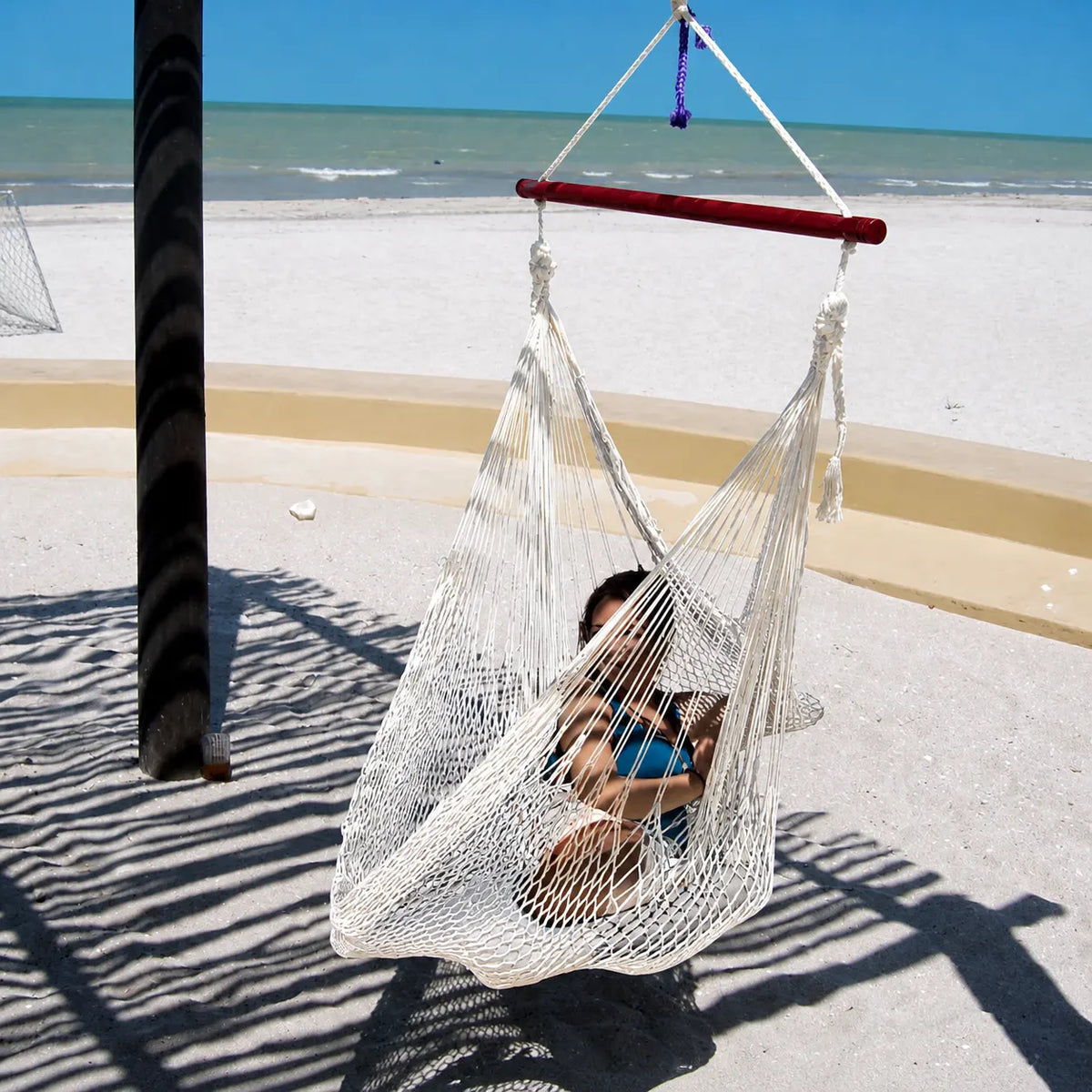 Person sitting in a hammock on a sandy beach with ocean view