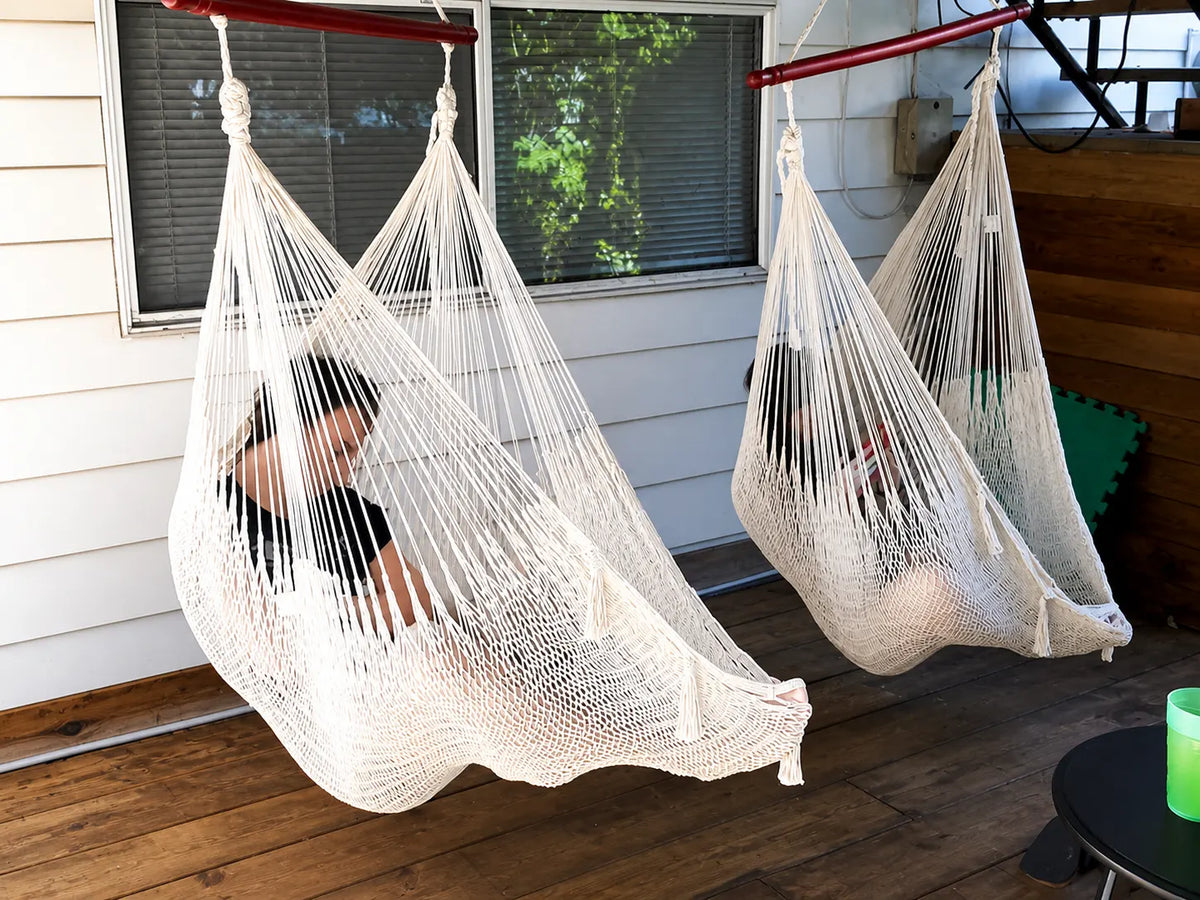 Two people sitting in white hammock chairs on a wooden floor.