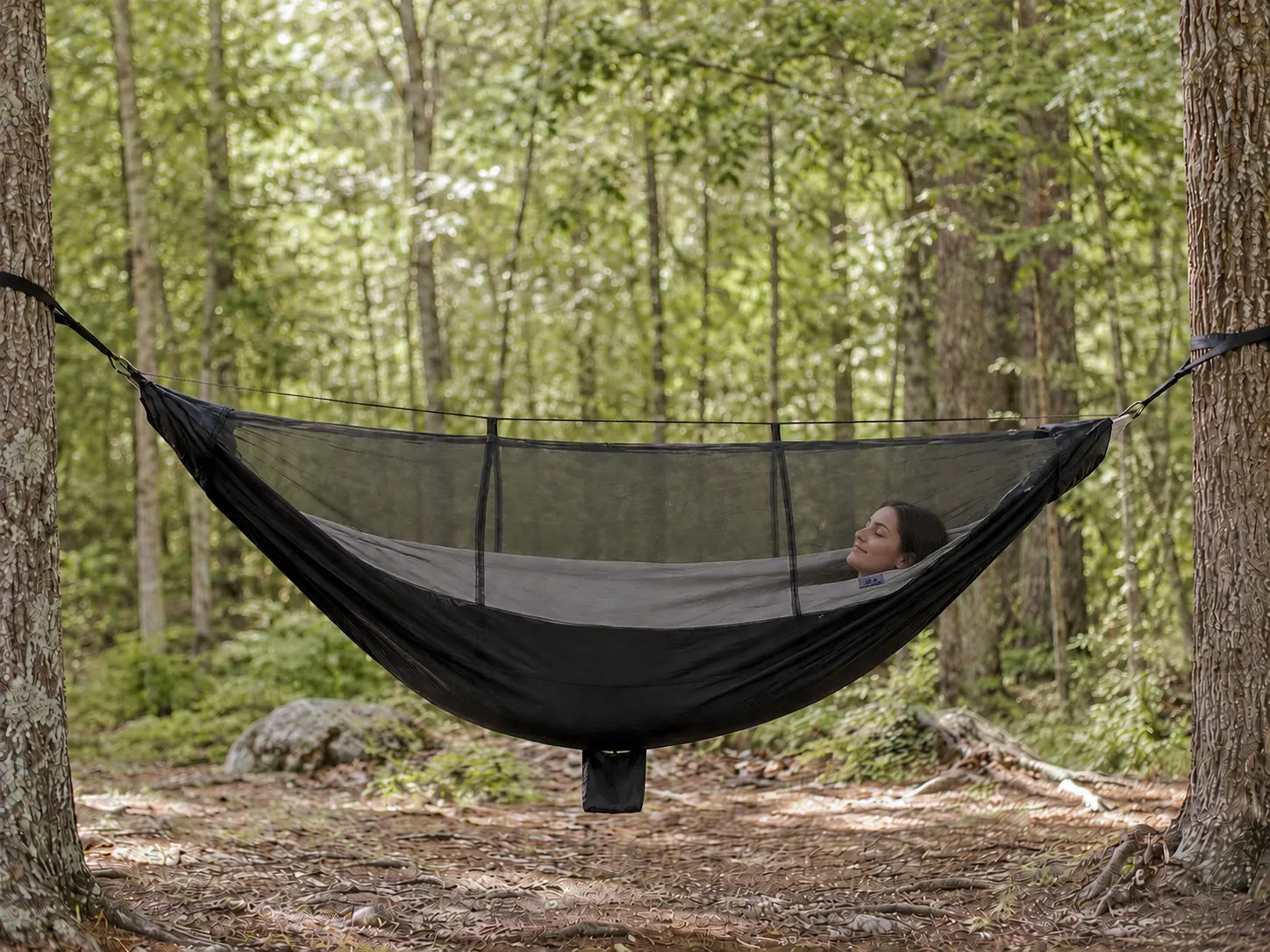 Person relaxing in a hammock with mosquito net in a forest setting