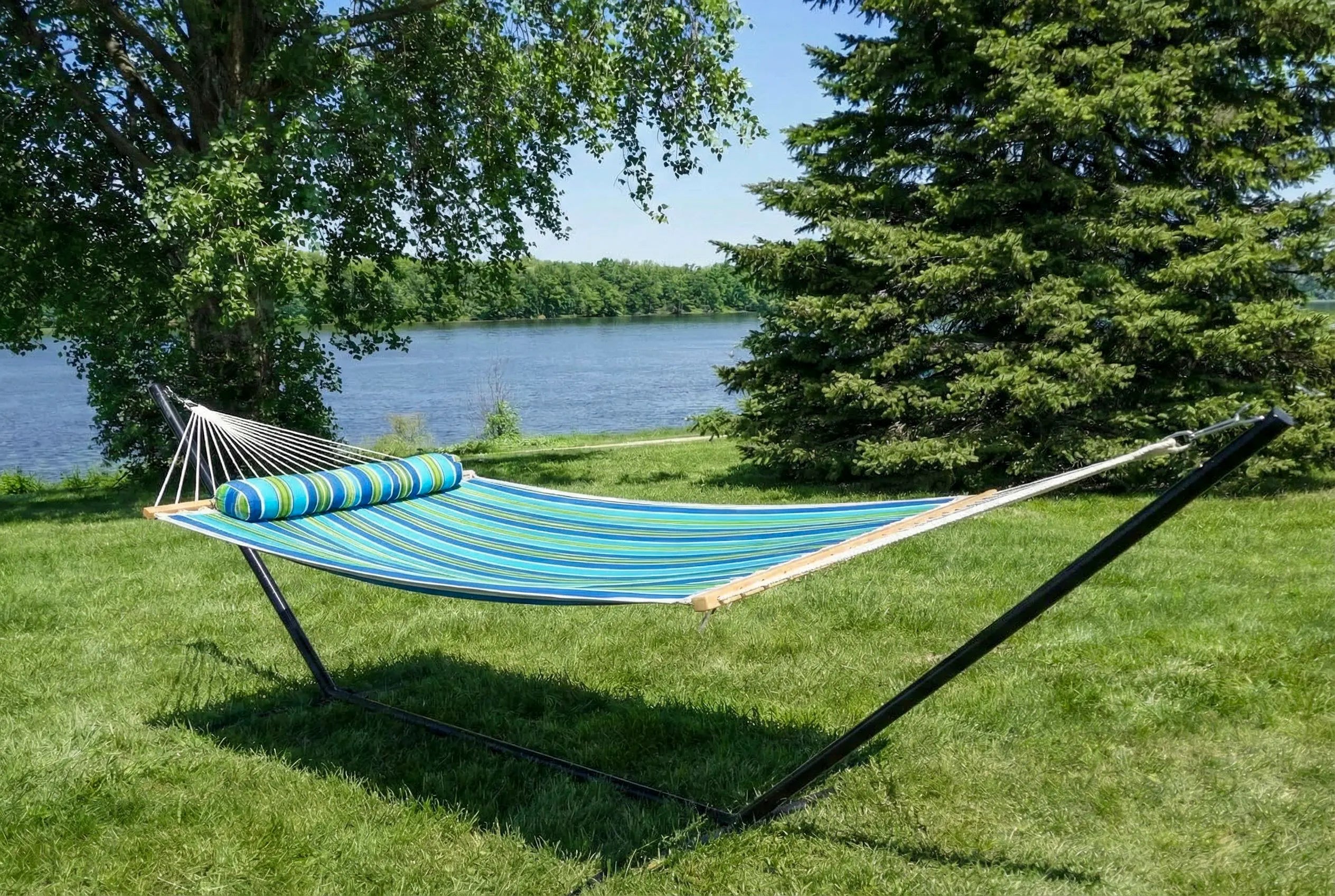 Blue hammock with striped pillow on a stand in a grassy area by a lake.  QHD-CAROLINA+15TBSB