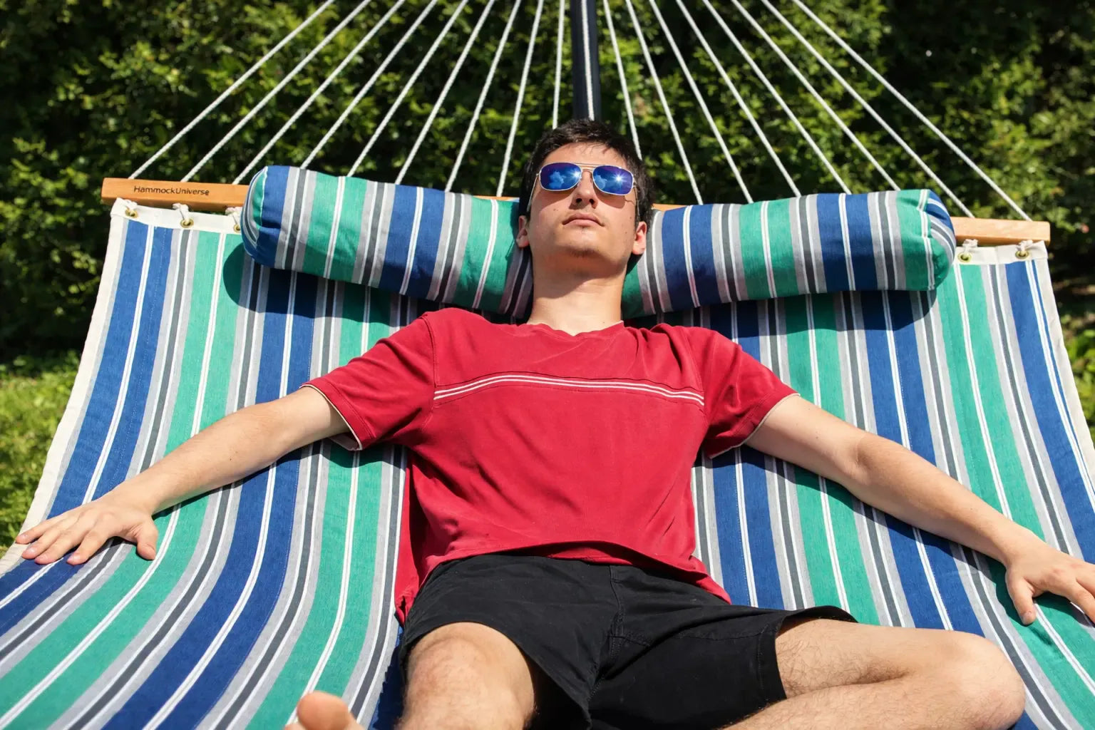 Man relaxing on a striped hammock with armrest pillows in a natural setting  QHD-GBGW+15TBSB