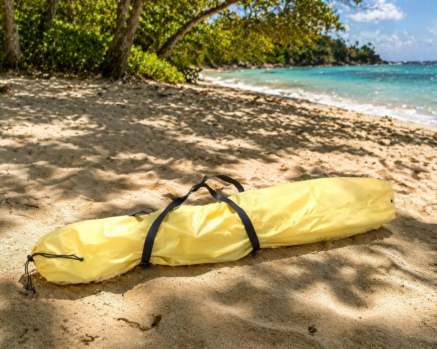Yellow hammock carrier bag on a sandy beach with ocean and trees in the background