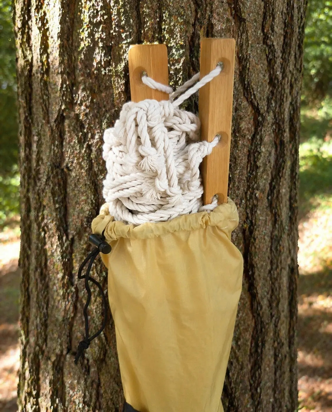 Rope tied to wooden planks attached to a tree with a yellow bag below, outdoors.