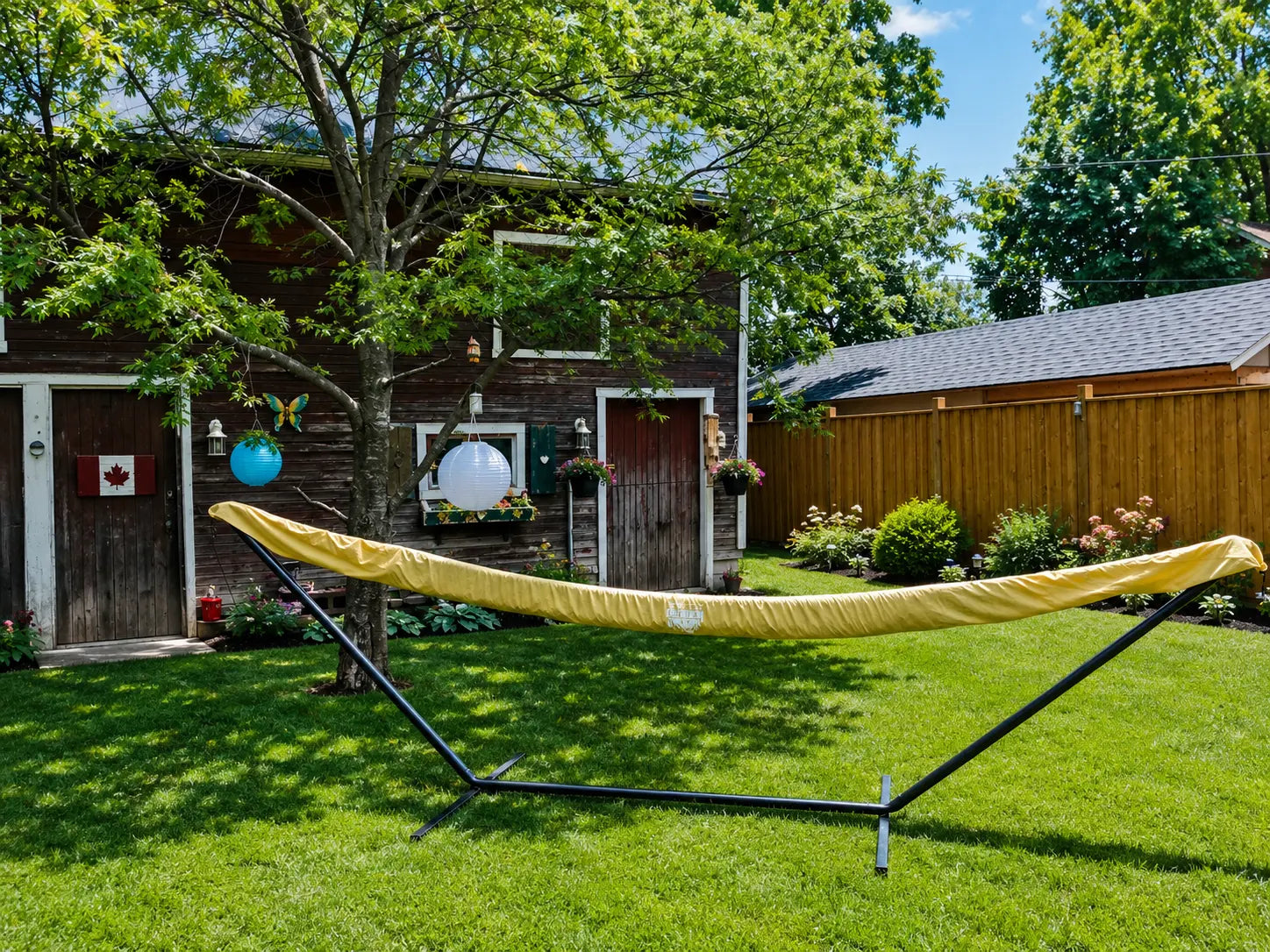 Yellow hammock on a stand in a backyard with a wooden cabin and trees in the background.